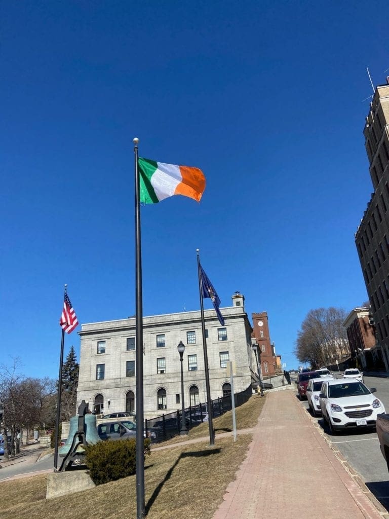 The American flag flies on the left, the Irish flag in the middle, and the Maine state flag on the right over Bangor Maine's city hall. 