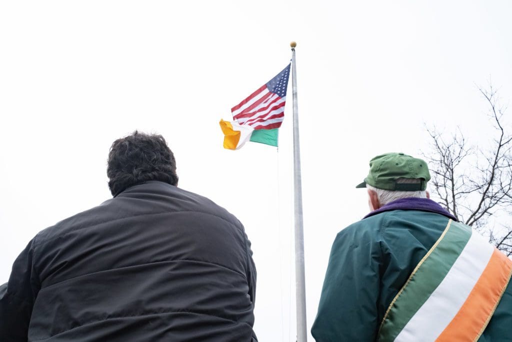 Two men stare up at the American and Irish flag flying